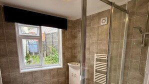 A bathroom with a shower, toilet, and sink, featuring herringbone flooring and a window with a view. - The Carlton Hotel (Shanklin)