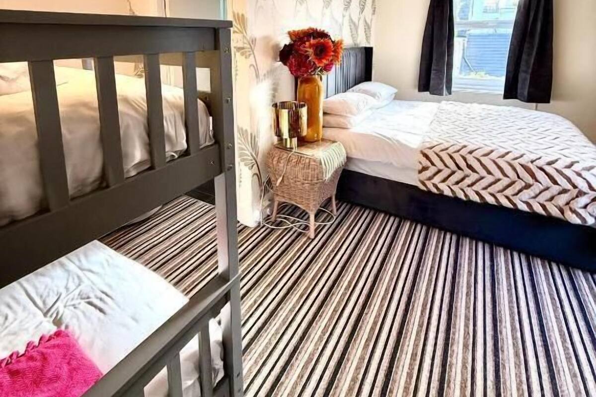 A hotel room with a bunk bed, a small side table with a vase, a patterned carpet, and two pendant lights.