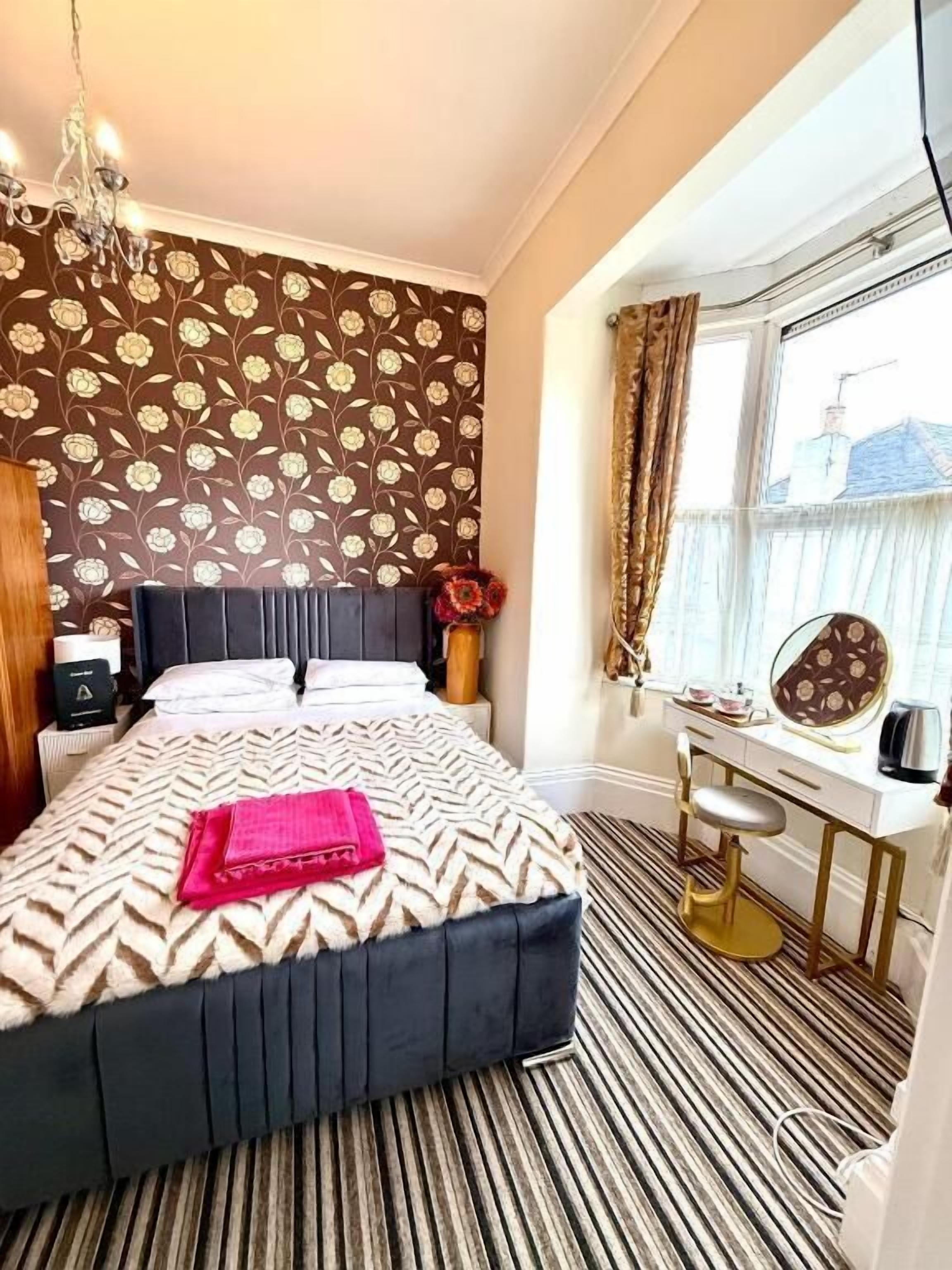 Una habitación de hotel con cama, tocador con espejo y ventana con cortinas.