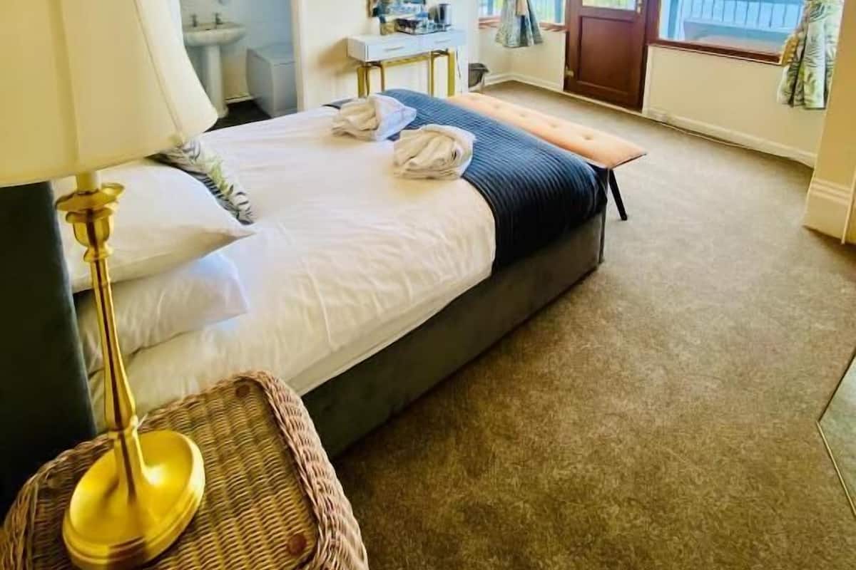 A hotel room with a bed, bedside lamp, wicker basket, and a view of the sea through large windows.