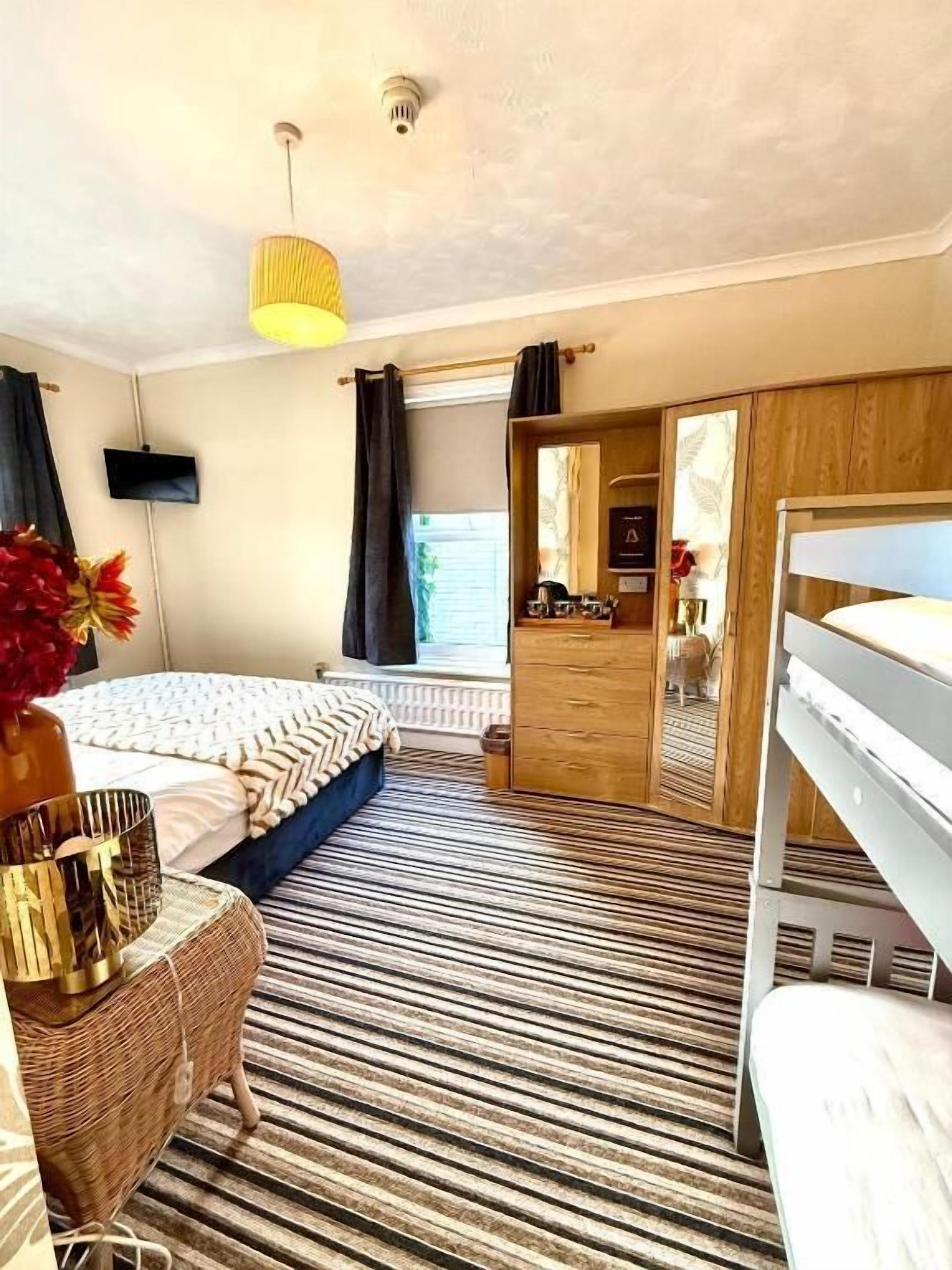A bedroom with a bed, a dresser, a mirror, a hanging light fixture, and a window with curtains.