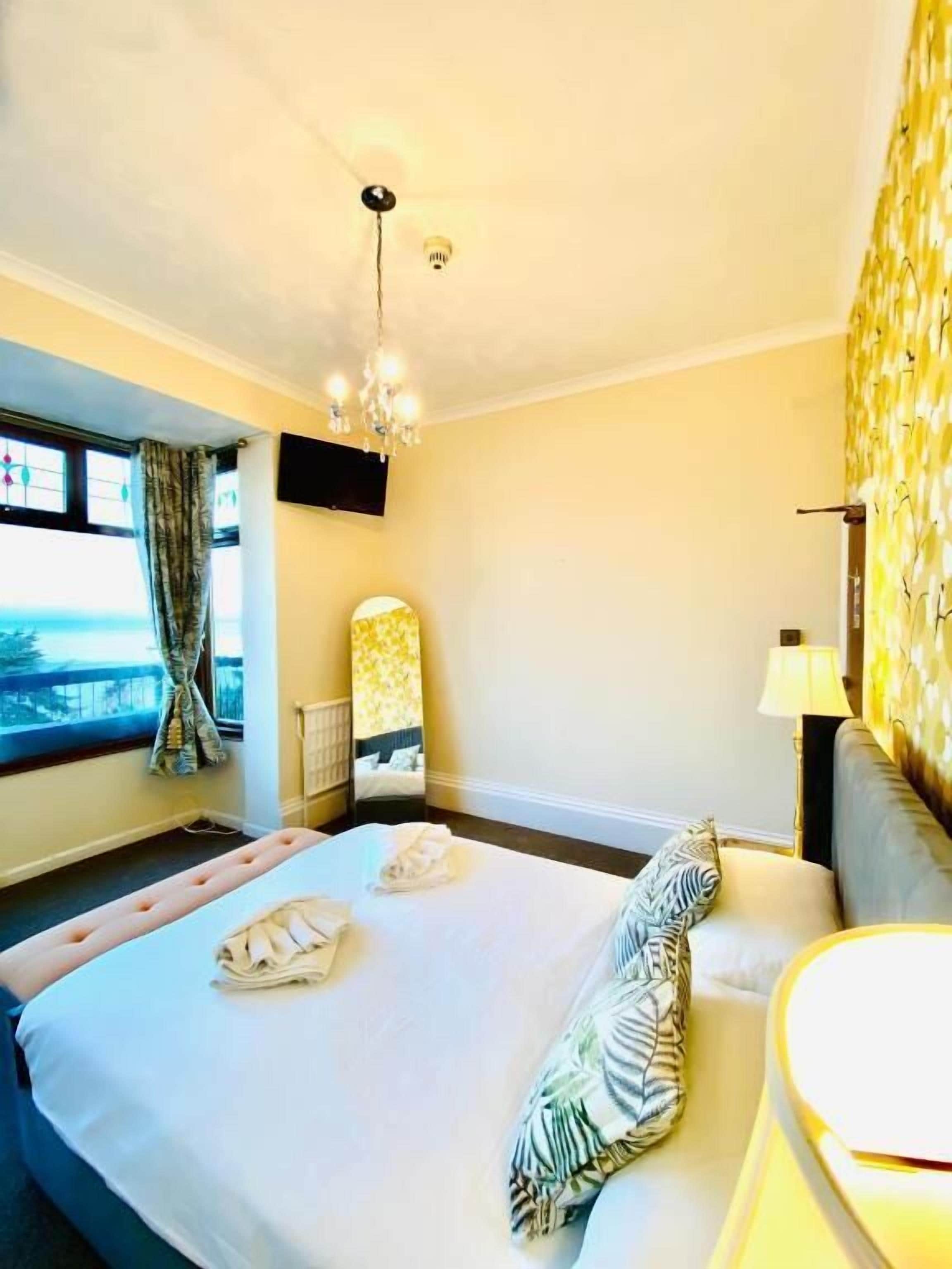 Une chambre d’hôtel avec un lit, un téléviseur fixé au mur, une fenêtre avec des rideaux et un lustre.
