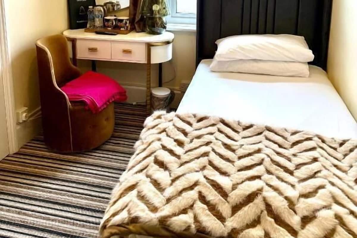 A hotel room with a bed, a desk, a chair, a window with curtains, and a rug.