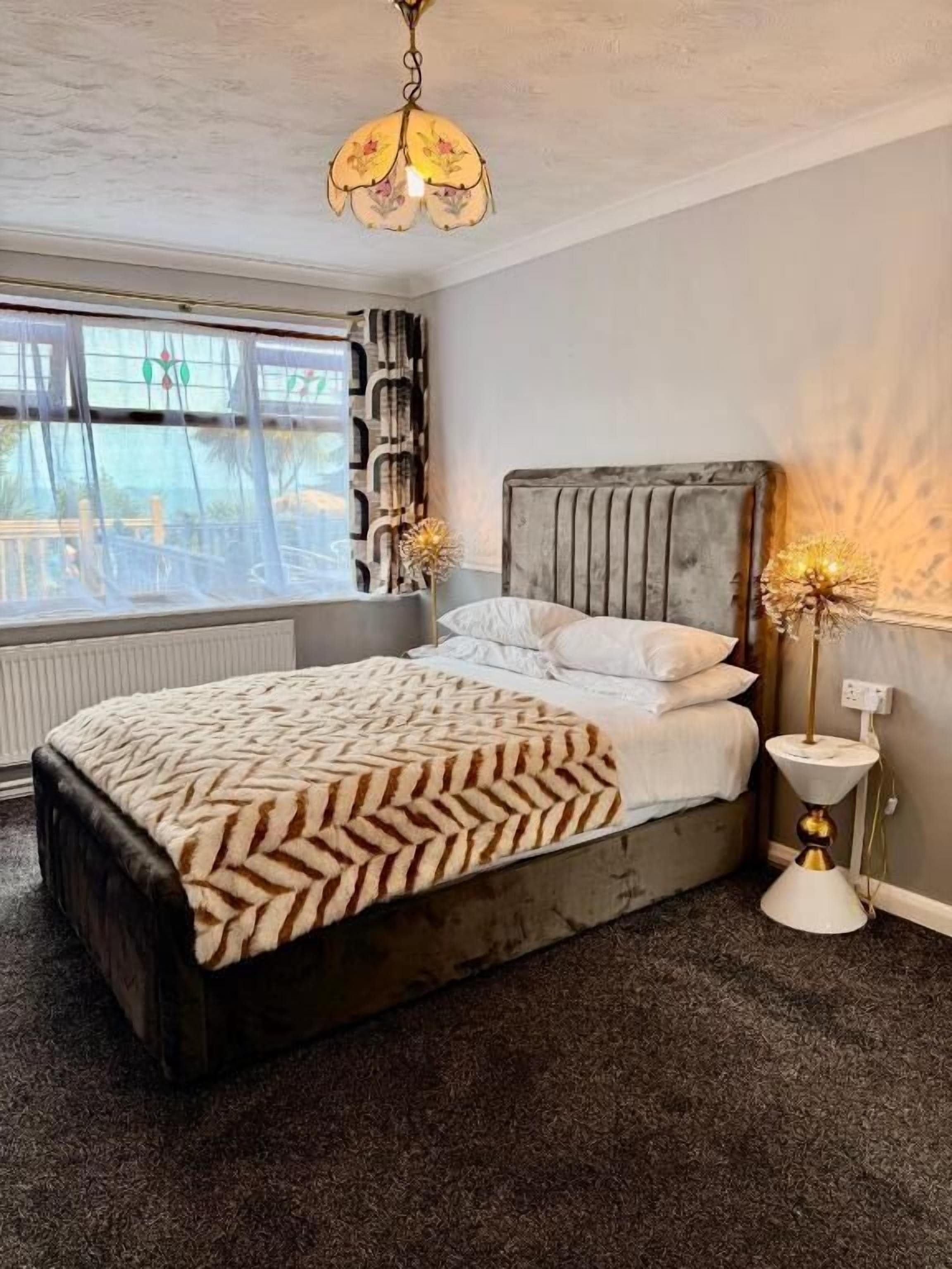 Une chambre à coucher avec un lit, une fenêtre avec des rideaux, un radiateur et une table de chevet avec une lampe.