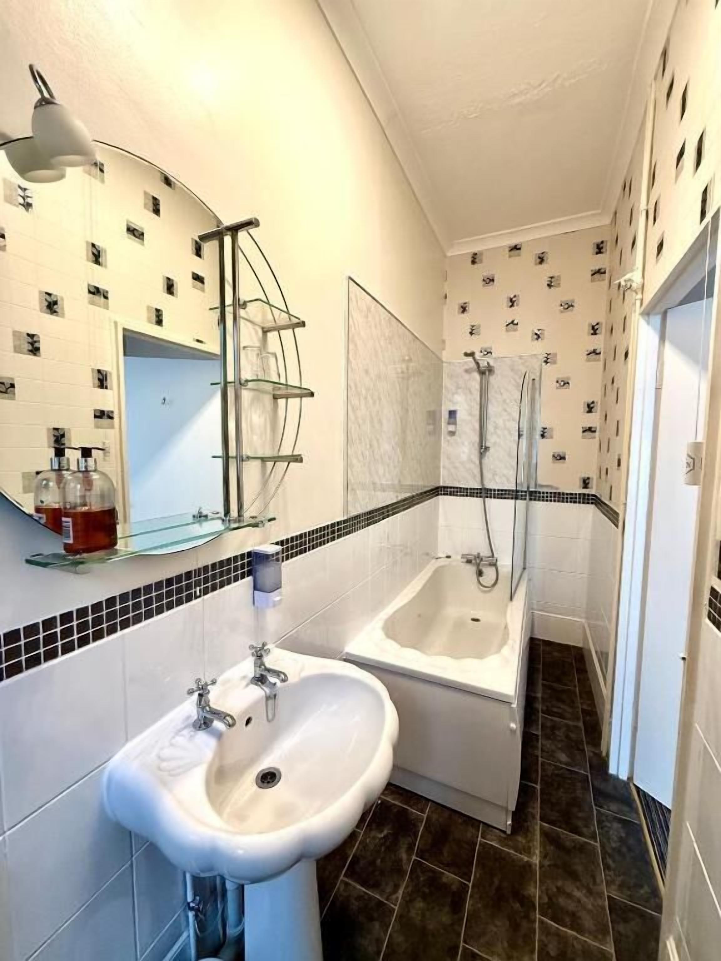 A bathroom with a sink, bathtub, and shower. There is a mirror above the sink and a towel rack. The walls have a patterned wallpaper.