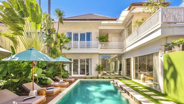 Ein modernes Haus mit Swimmingpool, Liegestühlen und tropischen Pflanzen.