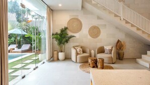 Ein modernes Wohnzimmer mit Glaswand, Treppe und Blick auf einen Pool.