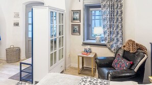 Ein Zimmer mit einem großen Bogenfenster, einem schwarzen Ledersessel, einem kleinen Tisch mit Lampe und einer weißen Tür mit Glasfeldern.