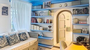 Ein gemütliches Zimmer mit einer Couch, Bücherregalen, einem Schreibtisch und einer Tür.