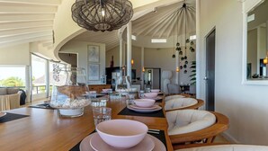 A dining area with a long table set for multiple people, chairs, and a hanging light fixture. - Villa Luna Del Sol l Unique Oceanview l Coral Estate Resort (Sint Willibrordus)