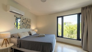 A bedroom with a bed, bedside lamps, a wall-mounted air conditioner, and a large window with curtains. - Villa Luna Del Sol l Unique Oceanview l Coral Estate Resort (Sint Willibrordus)