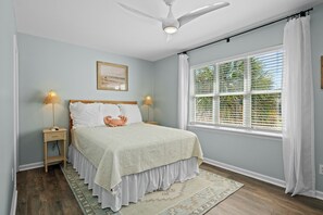 Une chambre à coucher avec un lit, des lampes de chevet, un ventilateur de plafond, une fenêtre avec des stores et un tapis.