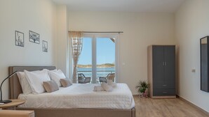A bedroom with a bed, a wardrobe, a chair, a small table, and a window with a view. - Studio 'Next To The Wave 1' with Sea View and Private Terrace (Μυρτιές)