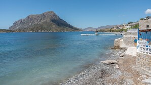 A coastal area with a rocky beach, a mountain in the background, and a pier with boats. - Studio 'Next To The Wave 1' with Sea View and Private Terrace (Μυρτιές)