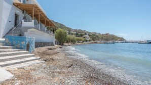 A coastal building with a staircase leading to a balcony, a pebble beach, and a clear blue sky. - Studio 'Next To The Wave 2' with Sea View and Private Terrace (Μυρτιές)