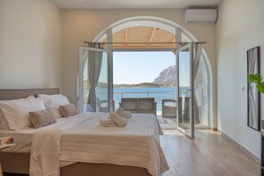 Ein Schlafzimmer mit einem großen Bett, Meerblick und einem Balkon mit Sitzgelegenheiten.