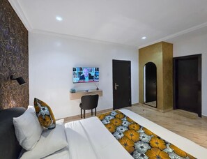 A modern hotel room with a bed, a desk, a TV, and a door. - Feliza Hotel And Suites  (Abeokuta)