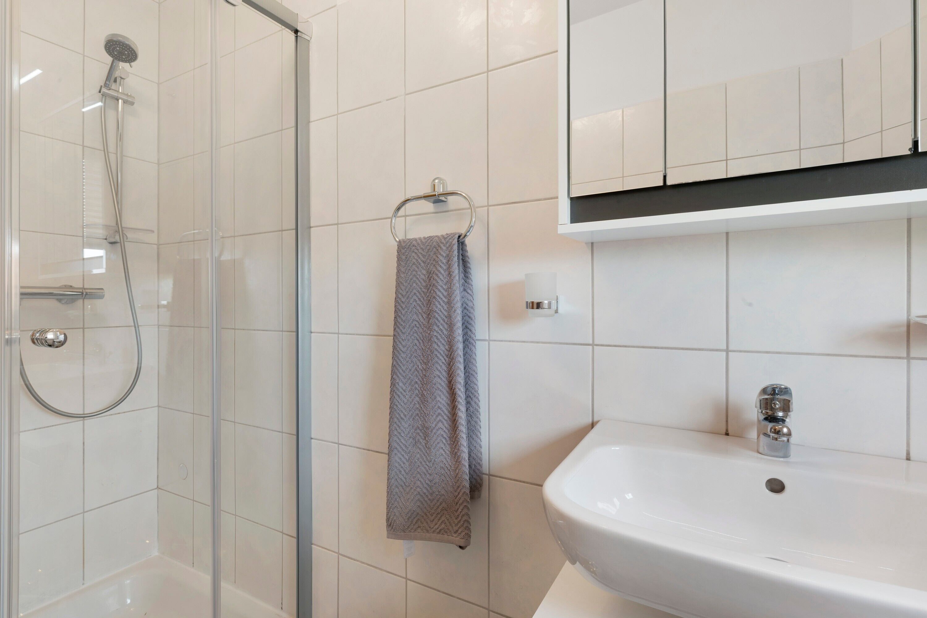 A bathroom with a glass-enclosed shower, a white sink, and a towel hanging on a rack.