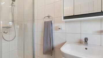 A bathroom with a glass-enclosed shower, a white sink, and a towel hanging on a rack.