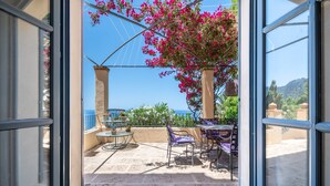 Une terrasse ouverte avec une table et des chaises, une vue sur la mer et une pergola ornée de fleurs roses.