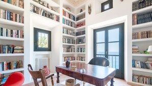 Une bibliothèque avec des étagères, une table en bois, une chaise rouge et une fenêtre.
