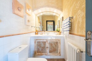 Ein Badezimmer mit einer weißen Toilette, einem Waschbecken mit Spiegel darüber, einem Handtuch auf einem Halter und einem Heizkörper an der Wand.