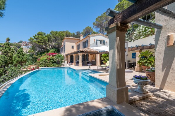 Ein Pool mit Pergola, Gartenmöbeln und Blick auf eine Hügellandschaft mit Gebäuden.
