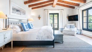 Une chambre à coucher avec un lit, des tables de chevet, une chaise, un téléviseur et une fenêtre avec des rideaux.