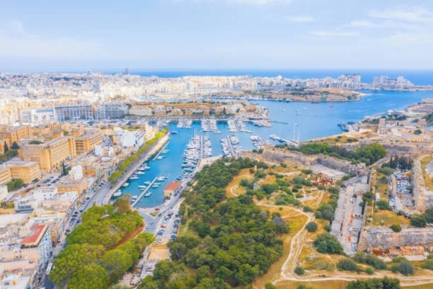 Vue aérienne d’une ville côtière avec un port de plaisance, des bâtiments et un mélange de paysages urbains et naturels.