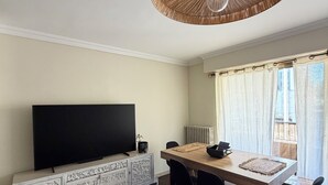 A dining area with a wooden table, black chairs, a TV on a white cabinet, and a large woven ceiling light. - 4-room apartment in the heart of Juan les Pins (Antibes)