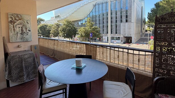 A balcony with a round table, chairs, a decorative painting, and a view of a modern building. - 4-room apartment in the heart of Juan les Pins (Antibes)