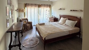 A bedroom with a bed, bedside tables, a desk, a chair, a lamp, a radiator, and a window with curtains. - 4-room apartment in the heart of Juan les Pins (Antibes)