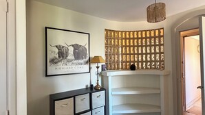 A hallway with a framed black and white photograph, a decorative wall panel, a white console table with drawers, a hanging lamp, and a rug on the floor. - 4-room apartment in the heart of Juan les Pins (Antibes)
