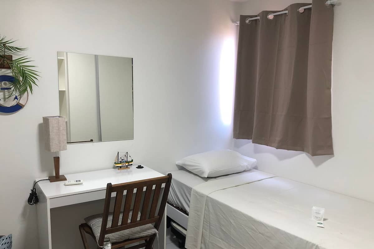 A small, single-bed room with a desk, chair, and a mirror.
