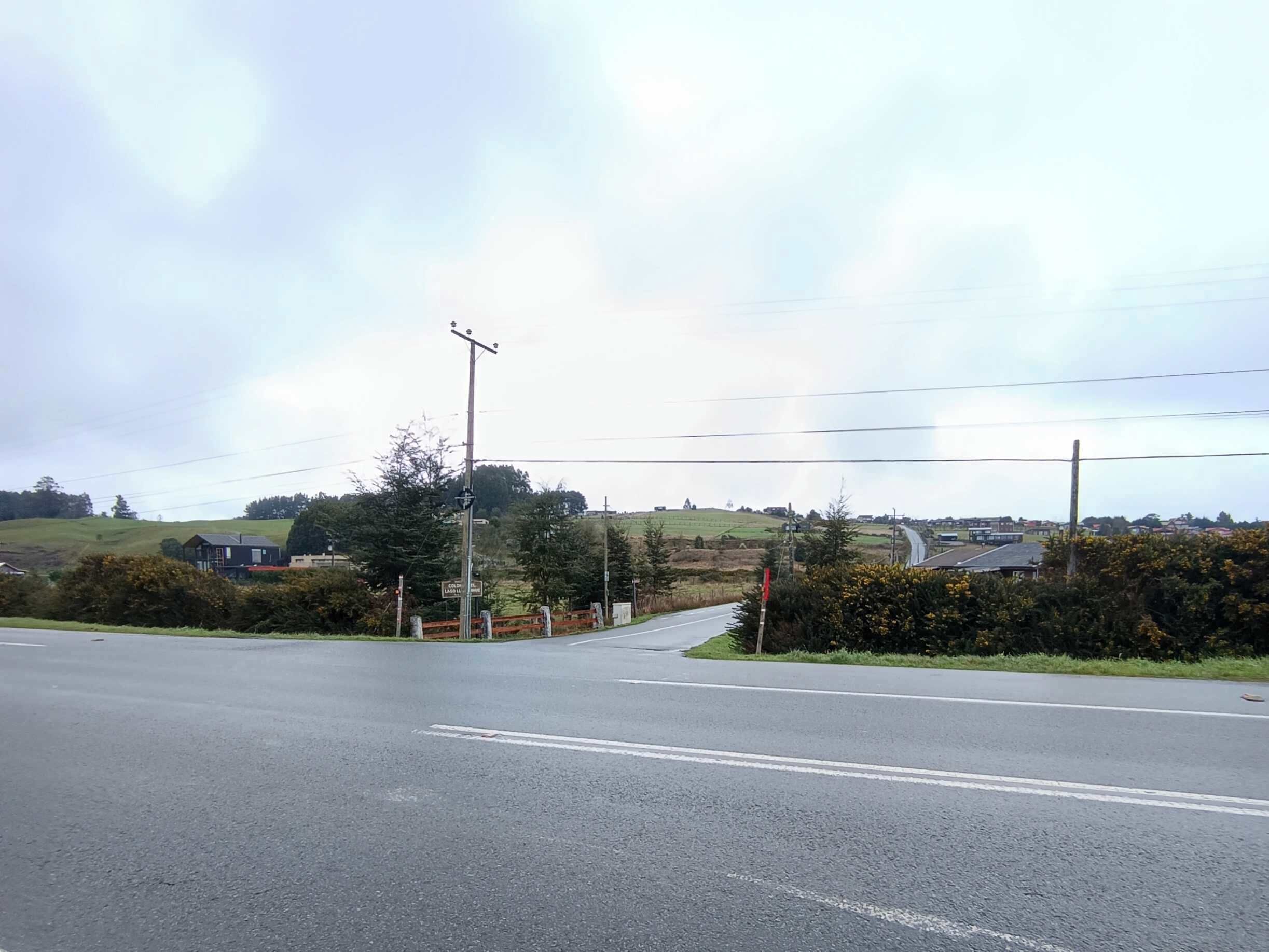 A rural road intersection with a traffic island, a pedestrian crossing, and a sign indicating a school zone.