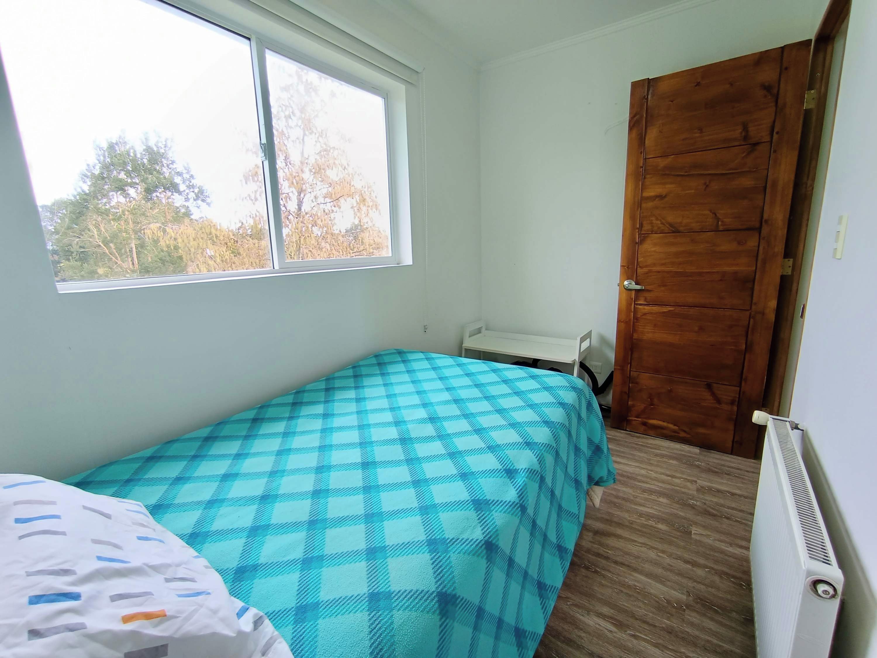 Een kleine kamer met een enkel bed, een houten deur, een raam en een radiator.