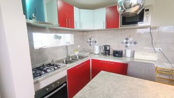 A kitchen with red cabinets, a gas stove, a microwave, and a coffee maker.