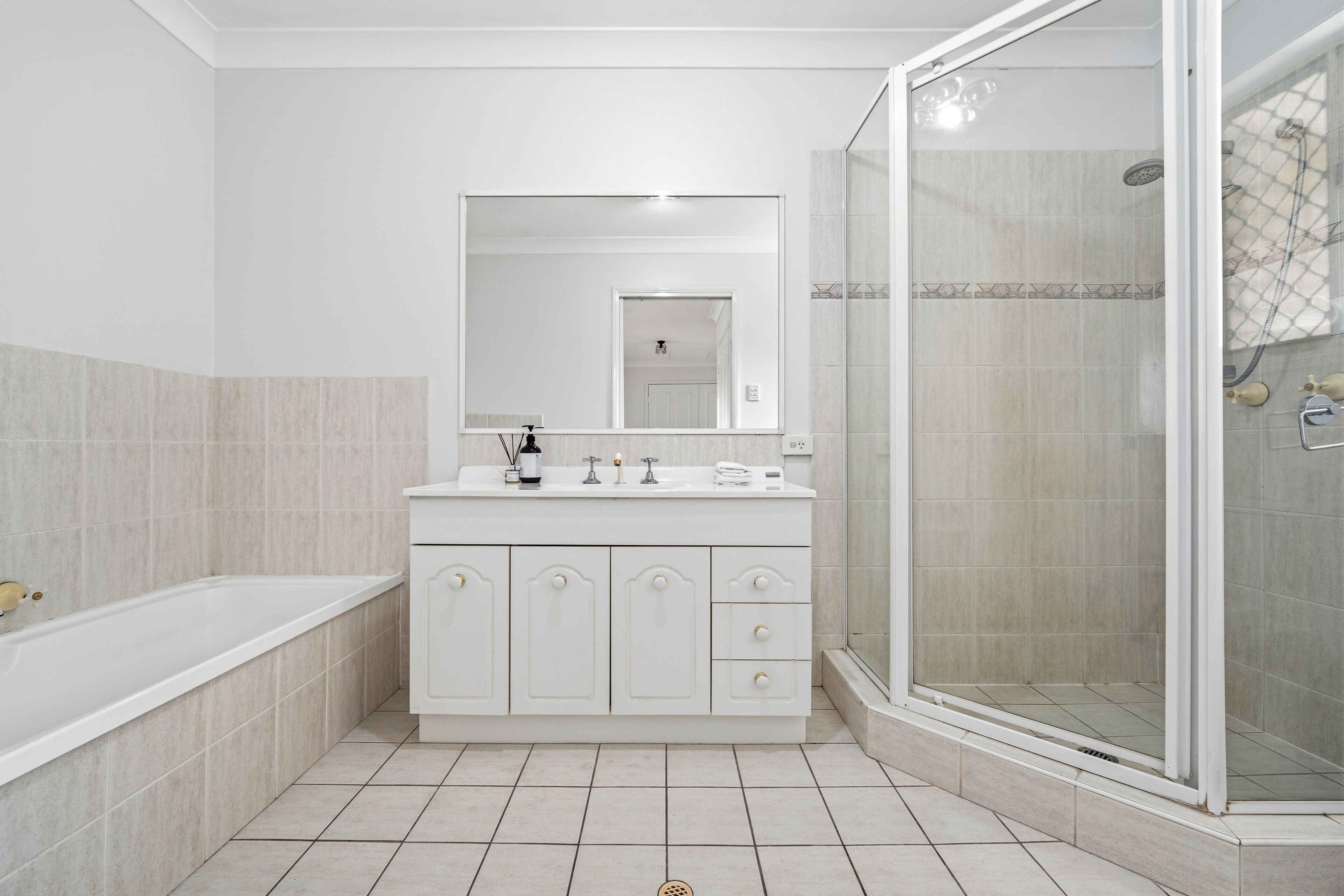 A bathroom with a bathtub, a shower, a vanity with a mirror, and tiled flooring.