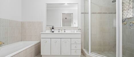 A bathroom with a bathtub, a shower, a vanity with a mirror, and tiled flooring.