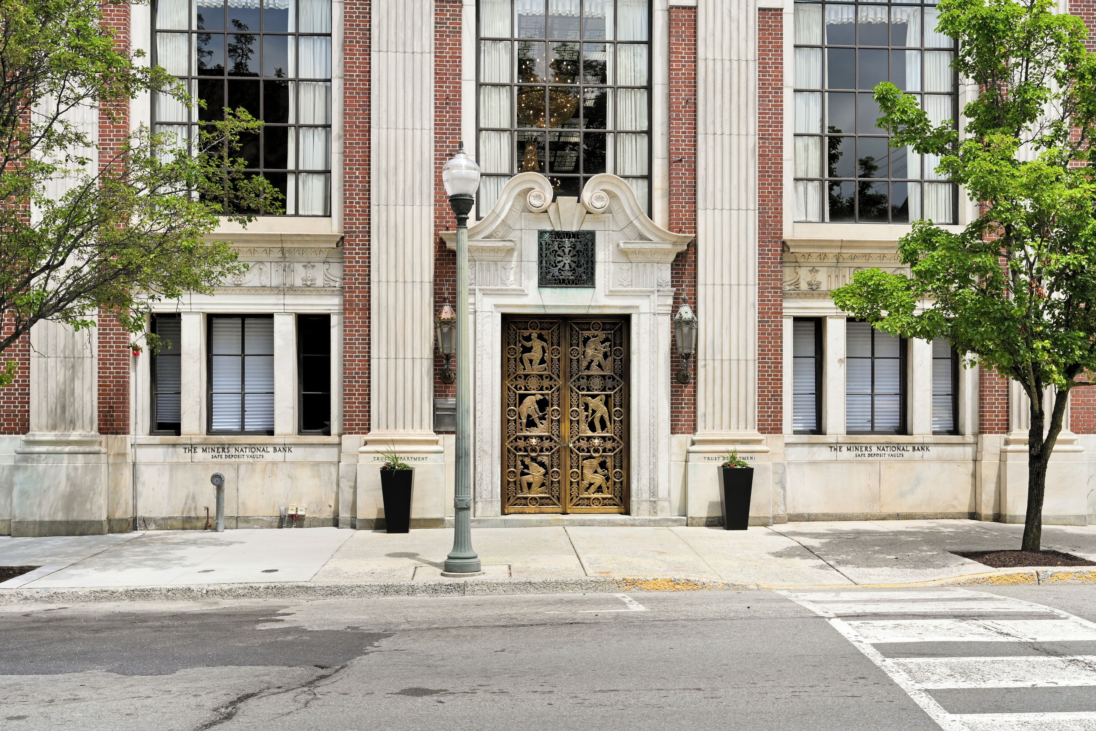 A building facade with a large ornate entrance, brick columns, and a sign reading 'The Miners National Bank.'