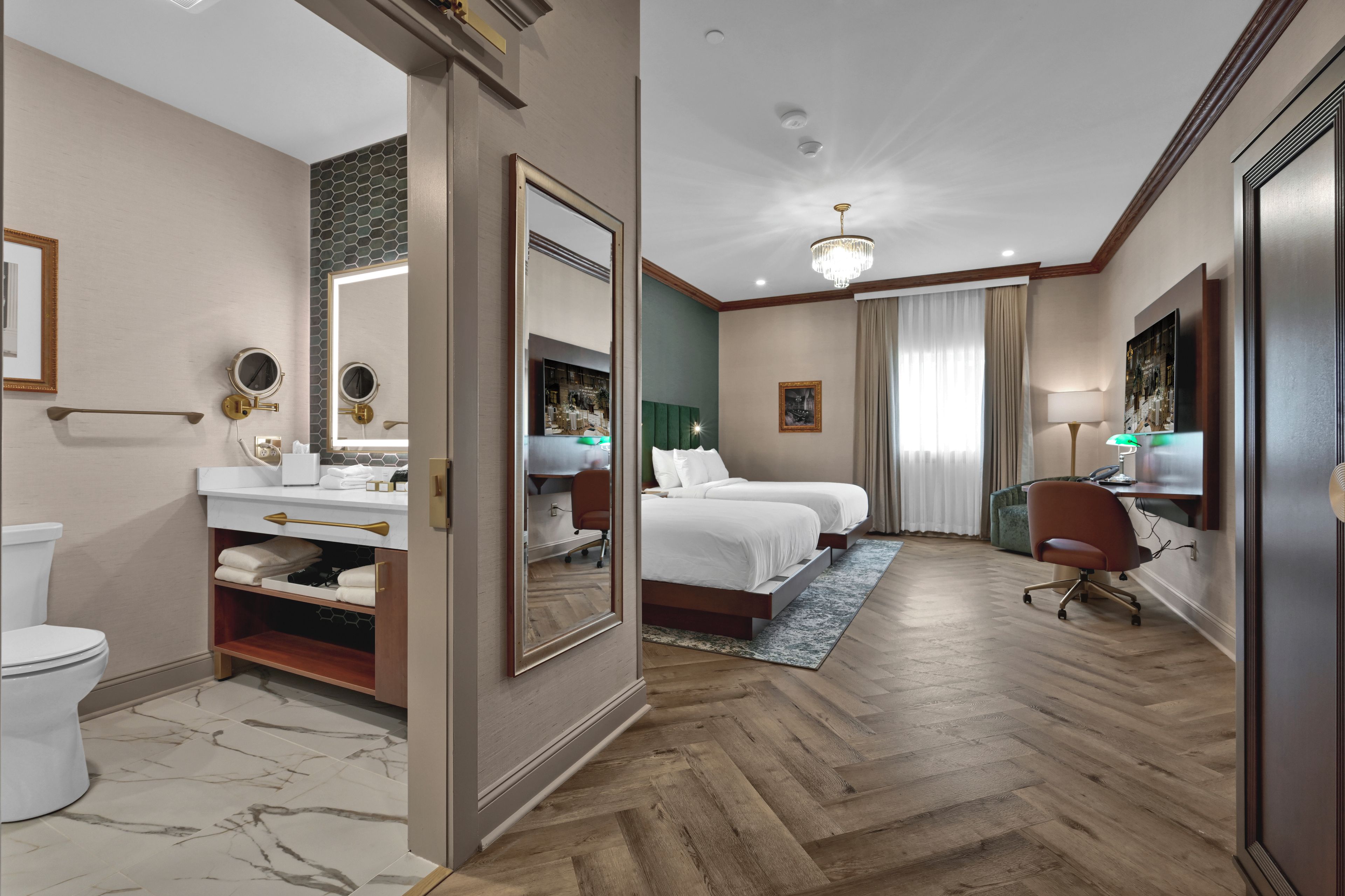 A hotel room with a large bed, a sitting area with a chair, a desk, and a bathroom with a toilet and sink.