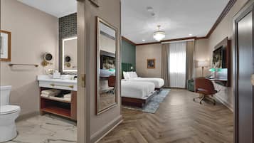 A hotel room with a large bed, a sitting area with a chair, a desk, and a bathroom with a toilet and sink.