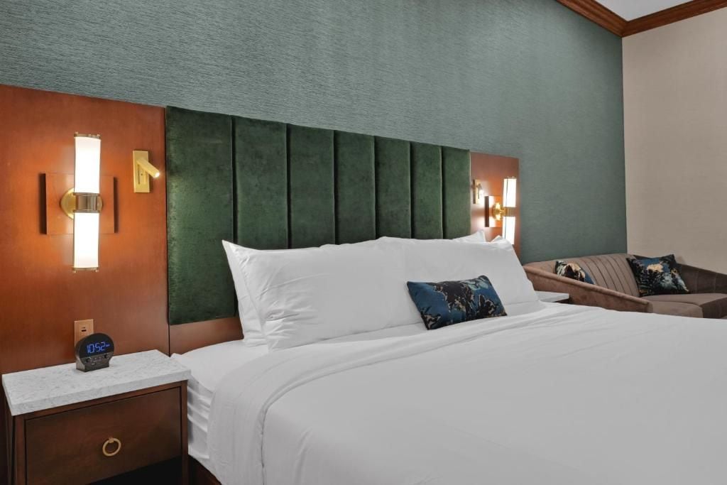 A hotel room with a large bed, a nightstand with a clock, and a wall-mounted light fixture.