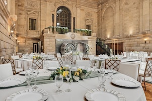 Un salón de banquetes con mesas redondas dispuestas para un evento formal, con manteles blancos, cristalería y centros de mesa florales.