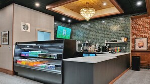 Zona de bar moderna con mostrador de bebidas, una máquina de café y una pizarra de menú.