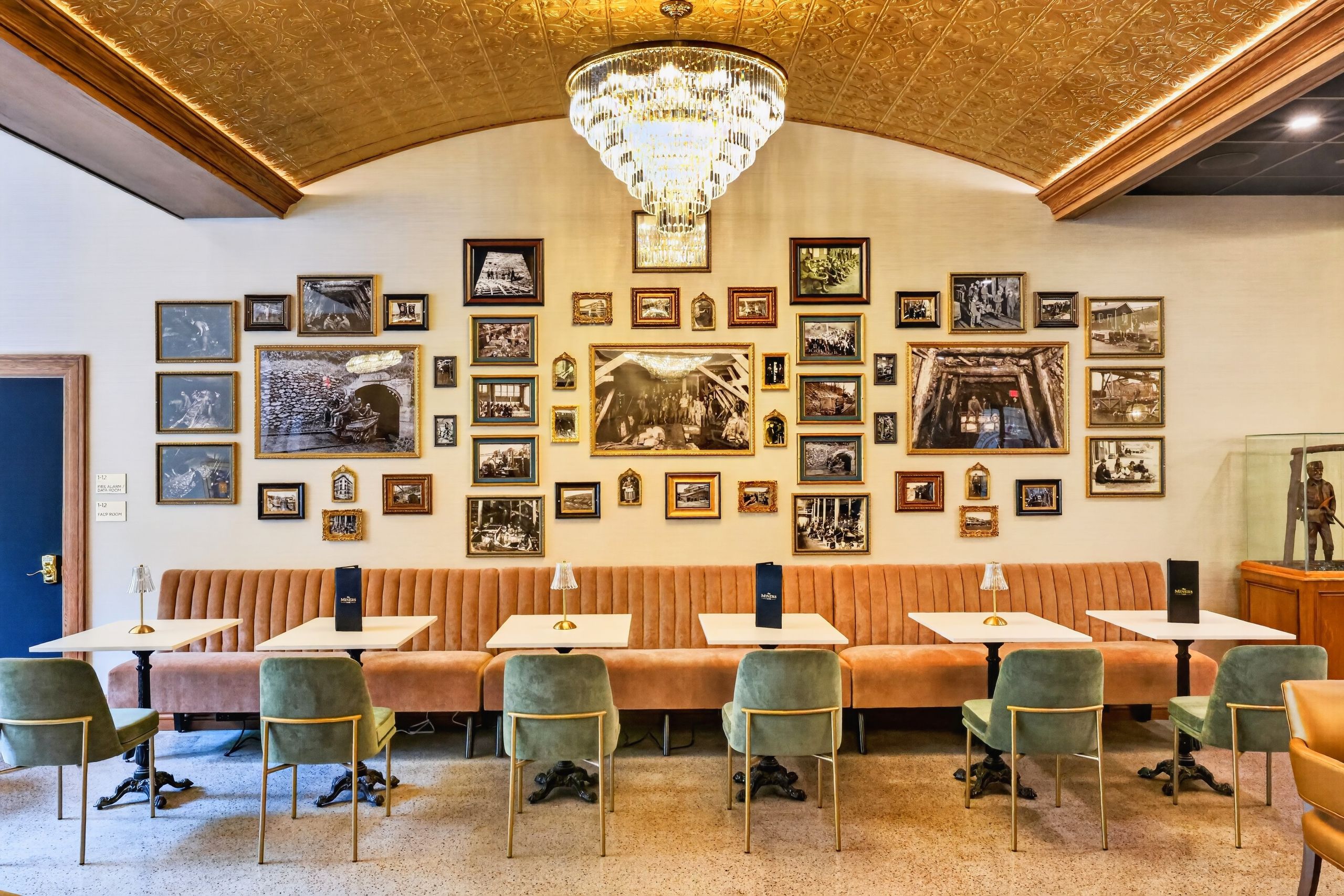 A restaurant with a high ceiling, ornate ceiling design, and a chandelier. Tables and chairs are arranged for dining.