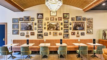A restaurant with a high ceiling, ornate ceiling design, and a chandelier. Tables and chairs are arranged for dining.