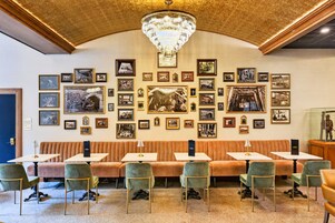 Un restaurante con techo alto, diseño ornamental en el techo y una araña. Mesas y sillas dispuestas para comer.