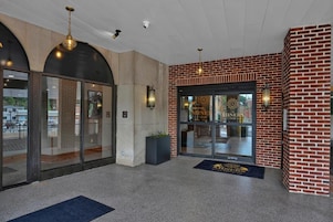 Un hall de hotel con entrada de vidrio, pared de ladrillo y alfombra azul.