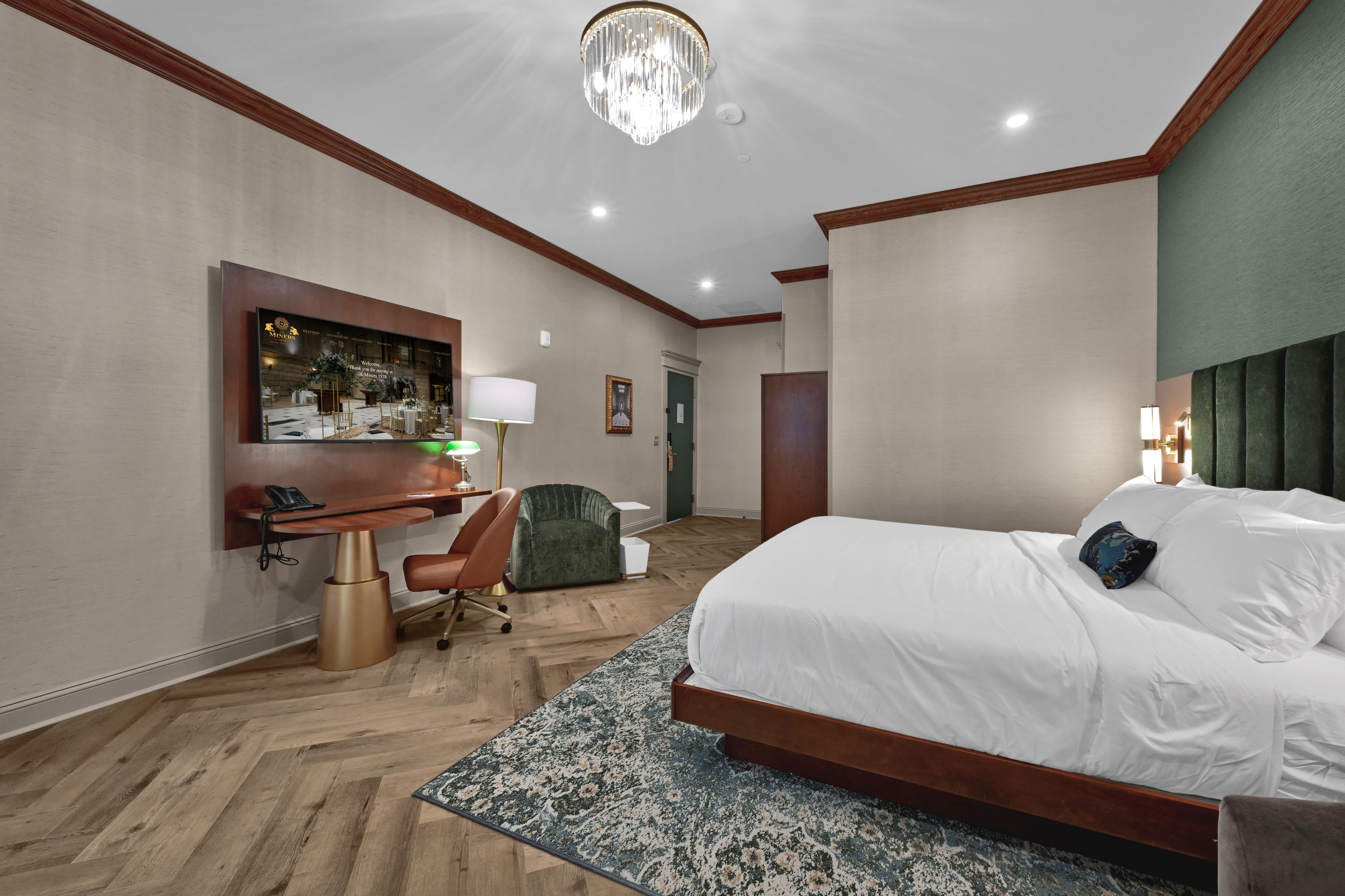 A hotel room with a large bed, a desk, a chair, a television, and a chandelier.